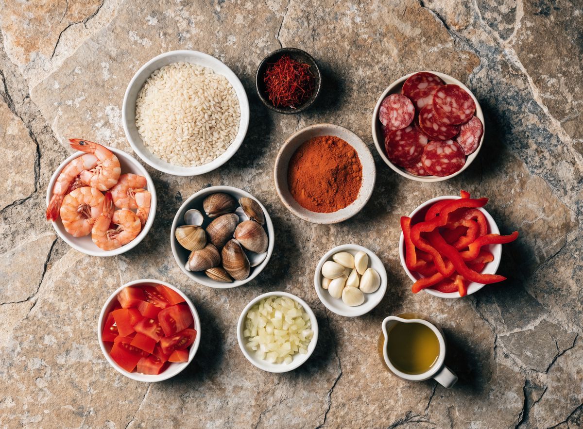 Nguyên liệu paella xếp trong các bát nhỏ: gạo bomba, nhụy nghệ tây, ớt bột, chorizo, tôm, ngao, cà chua, tỏi
